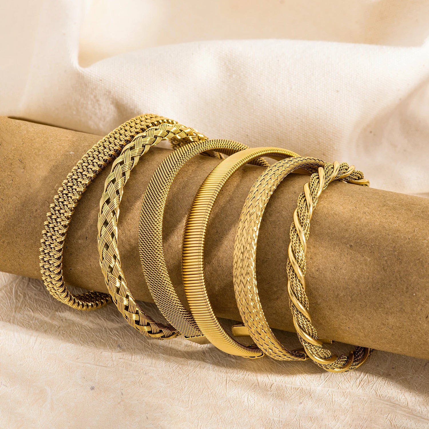 Gold open-end woven bangles with mixed textures, shown stacked on fabric