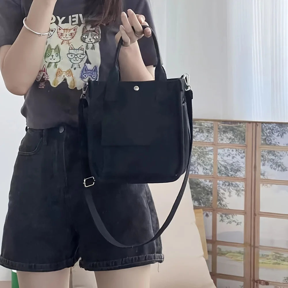 Black canvas tote bag with crossbody strap and front zipper pocket