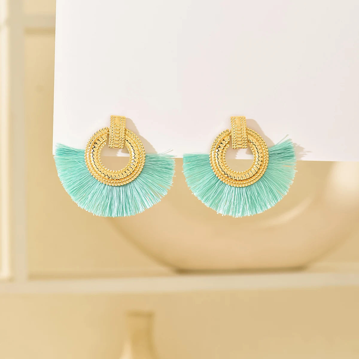 Gold fan stud earrings with mint tassels and circular geometric hoop detail