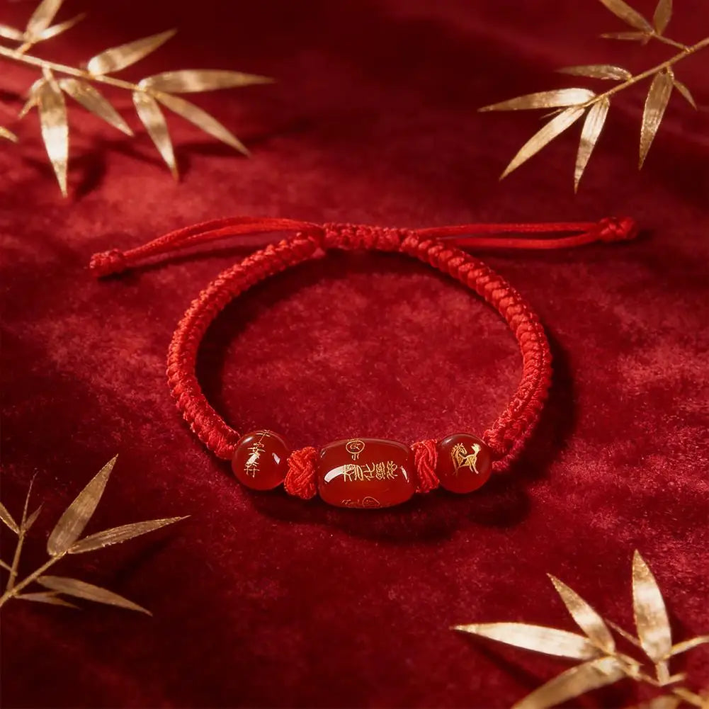 Red string bracelet with oval brown bead and small gold-tone symbol charms