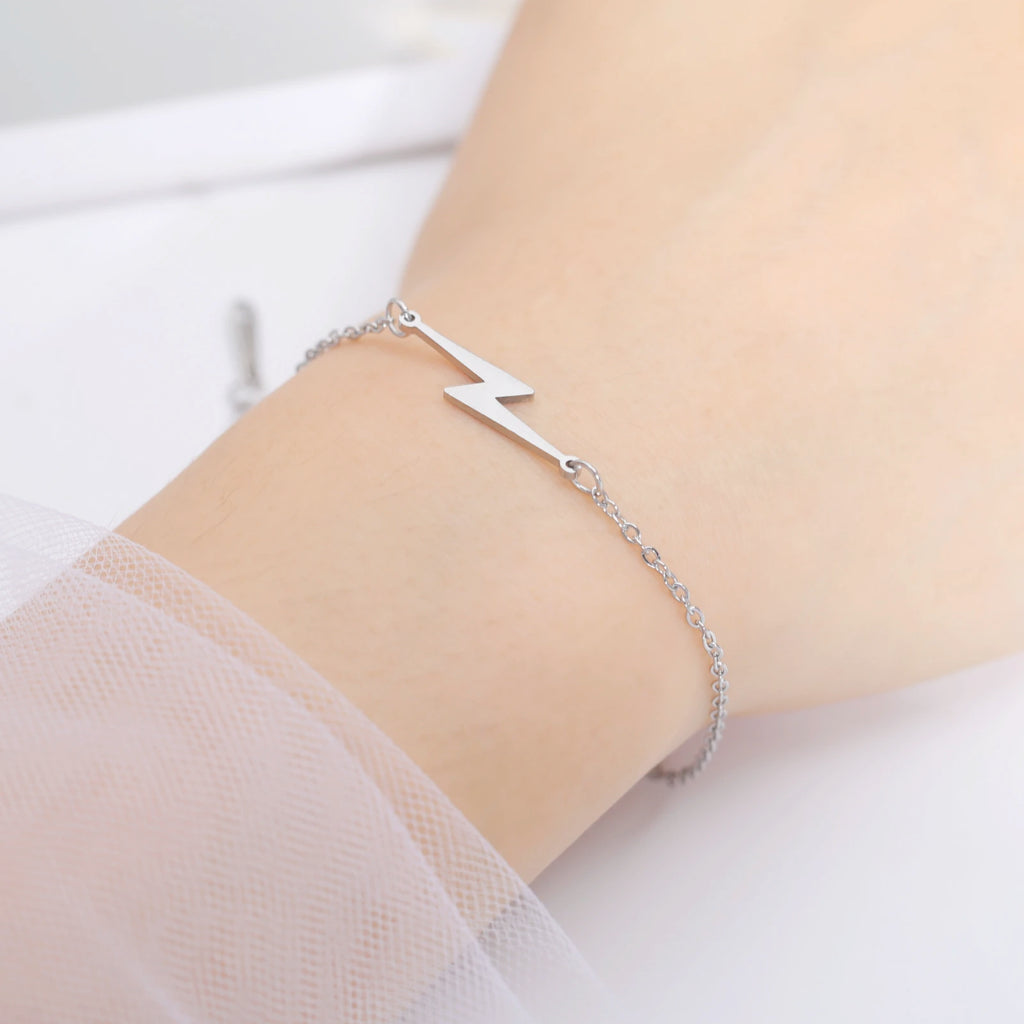 Silver tone lightning charm bracelet on wrist with small bolt pendant and chain links.