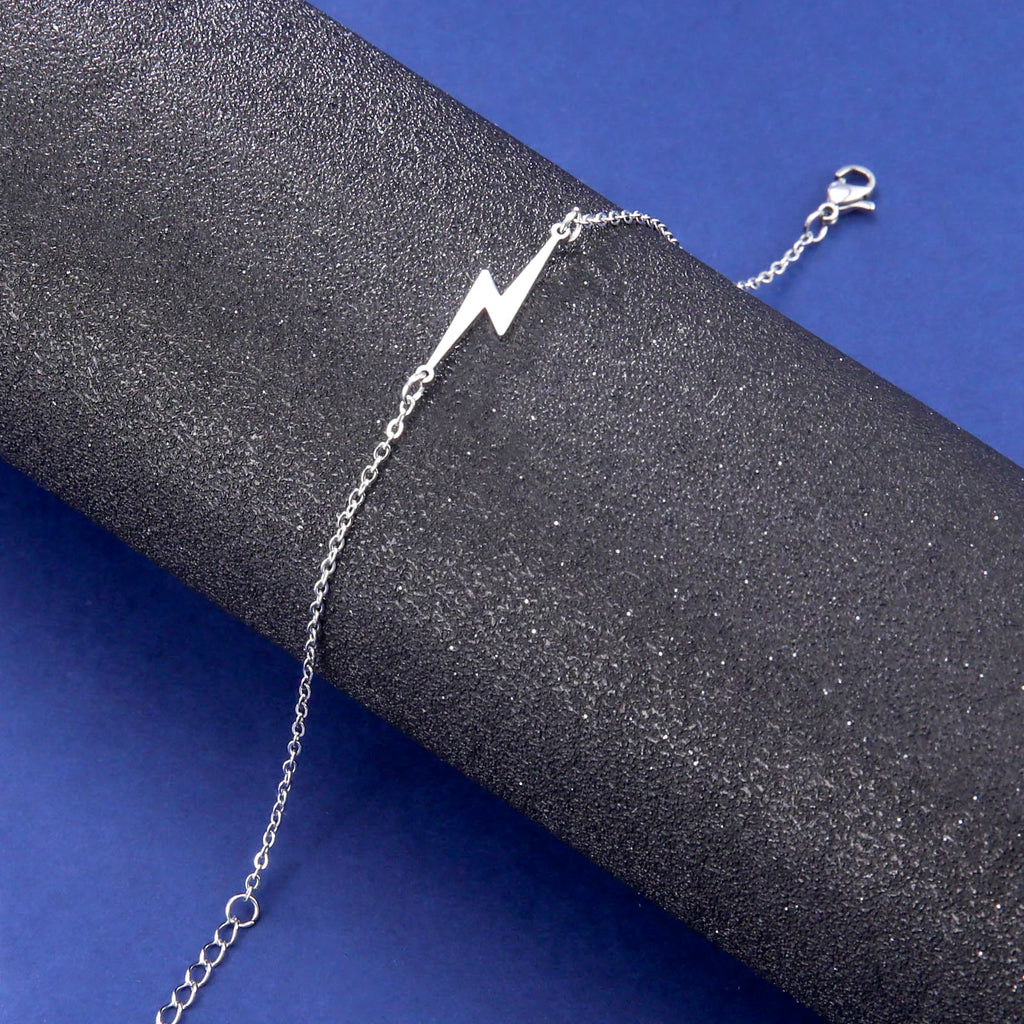 Silver tone lightning charm bracelet with long chain and white lightning bolt charm.