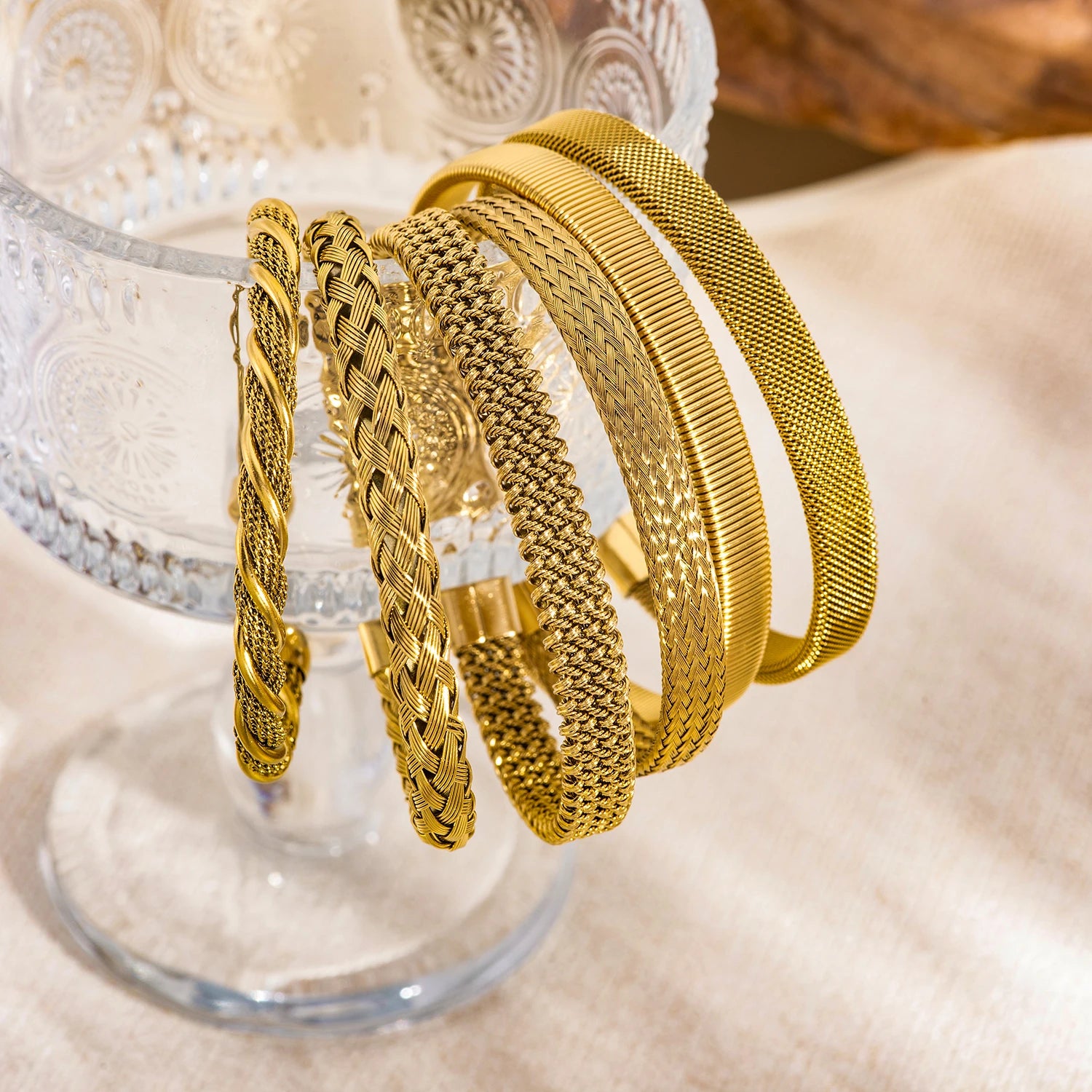 Gold textured open bangle bracelets on display, braided and mesh weave styles
