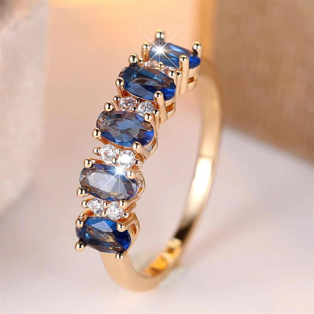 Gold-plated ring with three oval blue stones and clear round accents, prong set