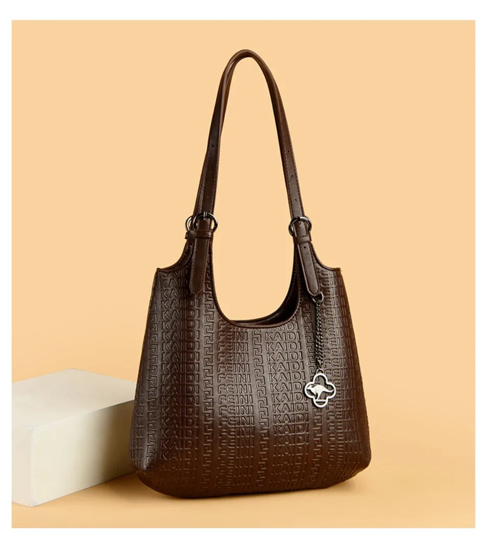 Dark brown leather shoulder bag with dual handles, embossed logo pattern, and clover charm