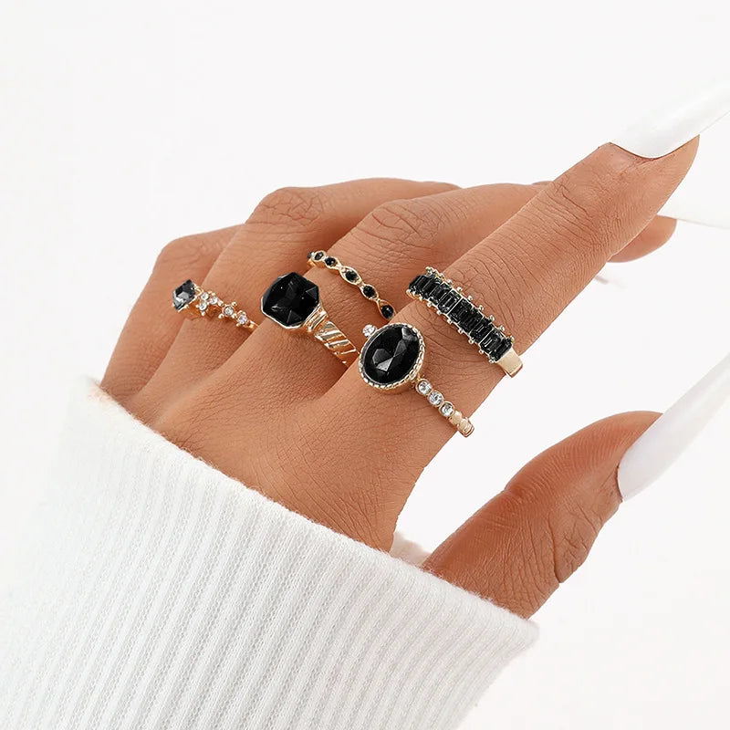 Gold-tone rings with black and green oval crystals and rhinestone accents on hand