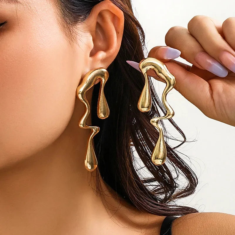 Gold irregular geometric drop earrings on ear, glossy abstract teardrop shapes
