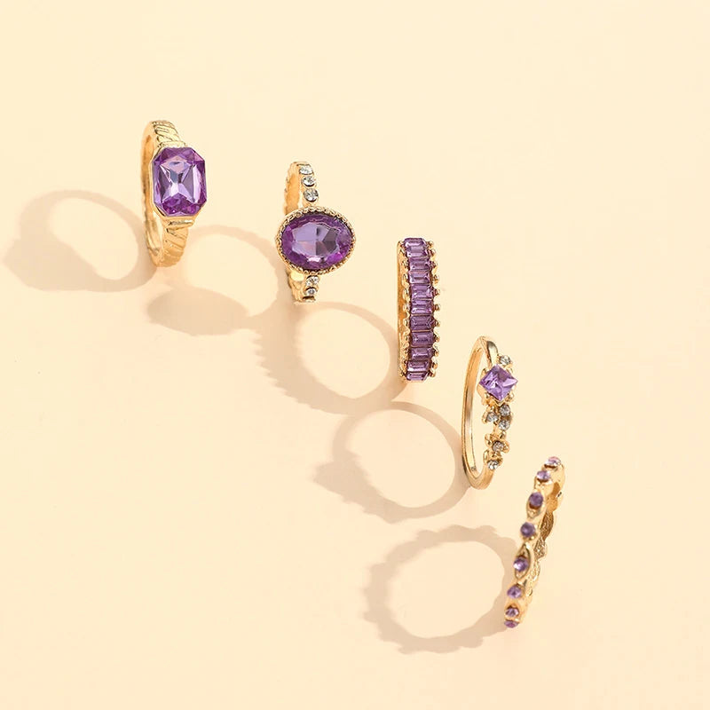 Gold-tone rings with purple crystal stones, including oval, baguette, and bar styles