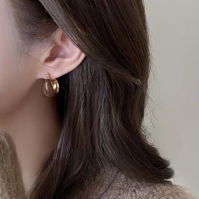 Gold-tone U-shaped hoop earrings with brown enamel teardrop accents, worn on ear