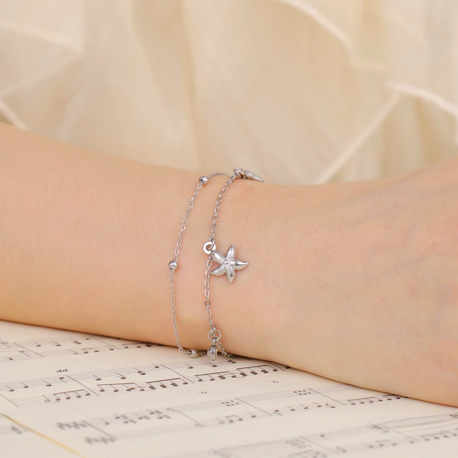 Silver-tone starfish and seashell charm bracelet on wrist with dangling starfish