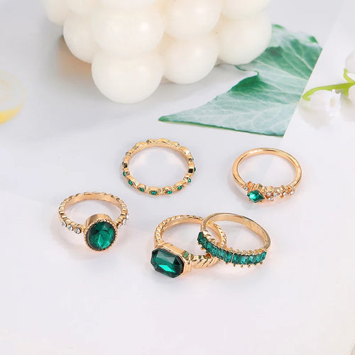 Five gold-tone rings with green crystals, including oval and band styles