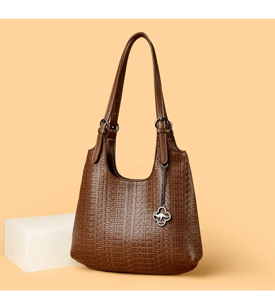Brown leather shoulder bag with dual handles, embossed logo pattern, and clover charm