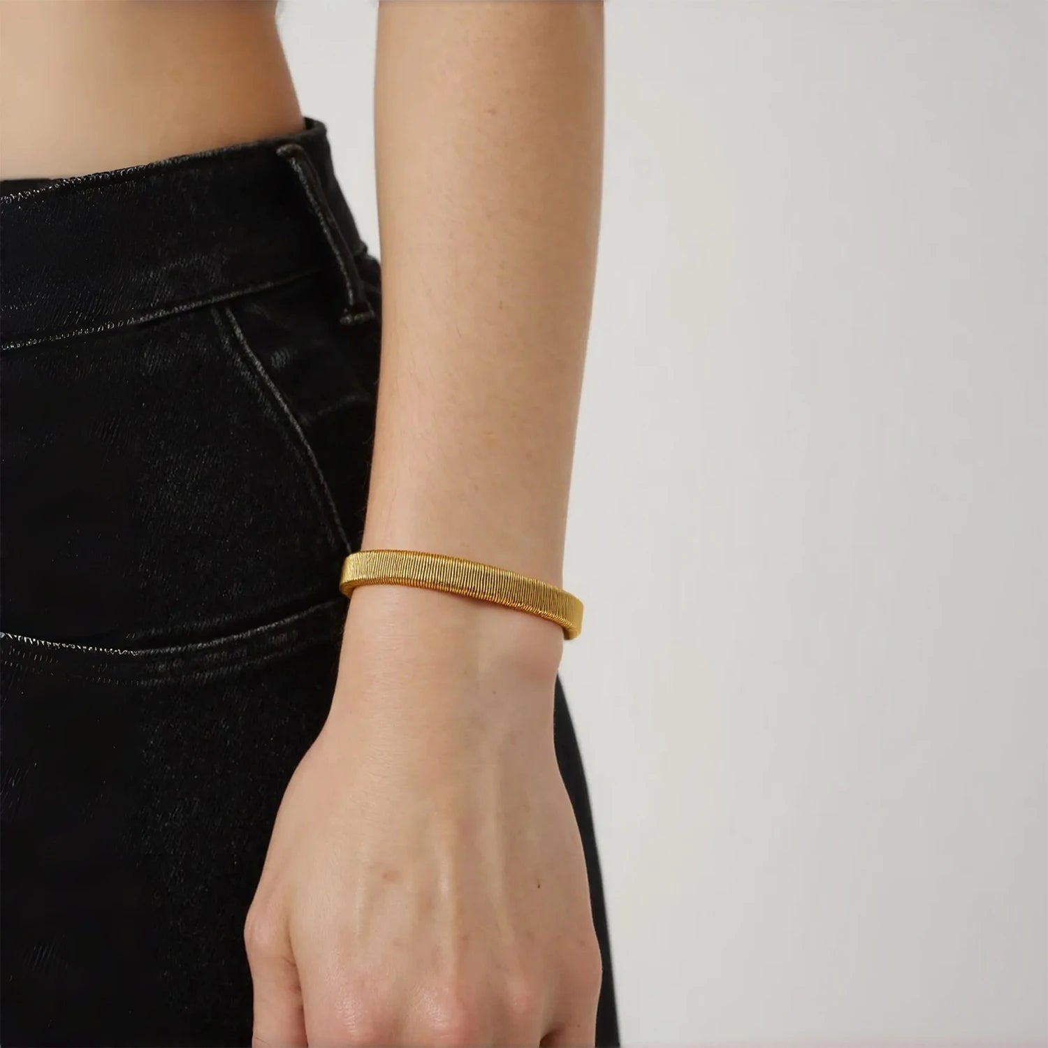 Gold tone open bangle bracelet on wrist, slim textured weave with squared ends
