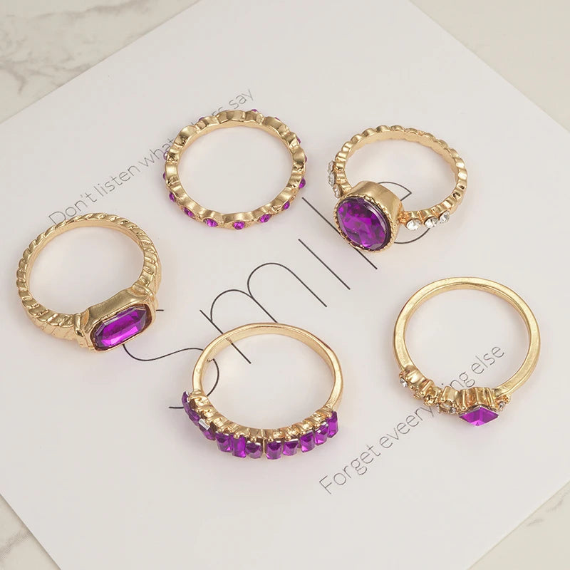 Gold-tone purple crystal rings on display card, showing several band designs