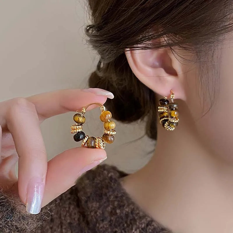 Gold-tone dangling U-hoop earrings with brown and black beaded drops, held by hand