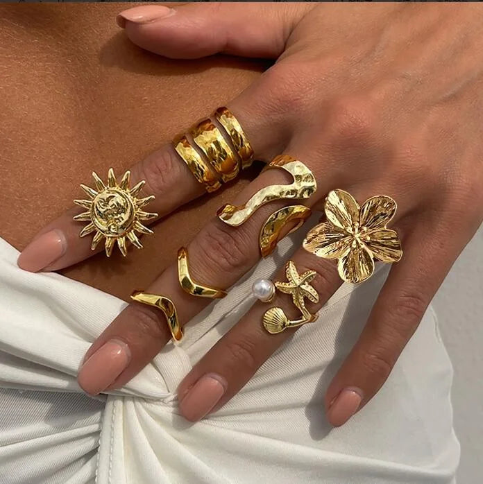 Gold-tone knuckle rings with sunburst, starfish, and flower charms plus pearl detail