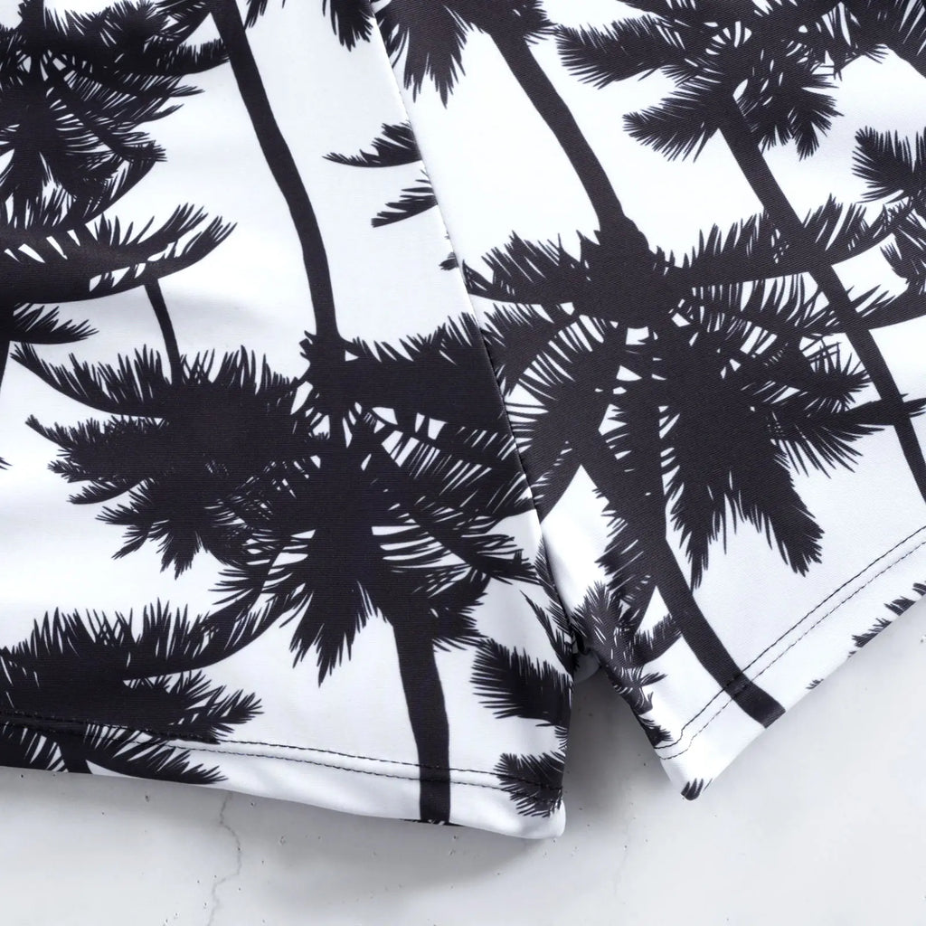 Palm-print swim shorts fabric close-up with drawstring cord and seams.