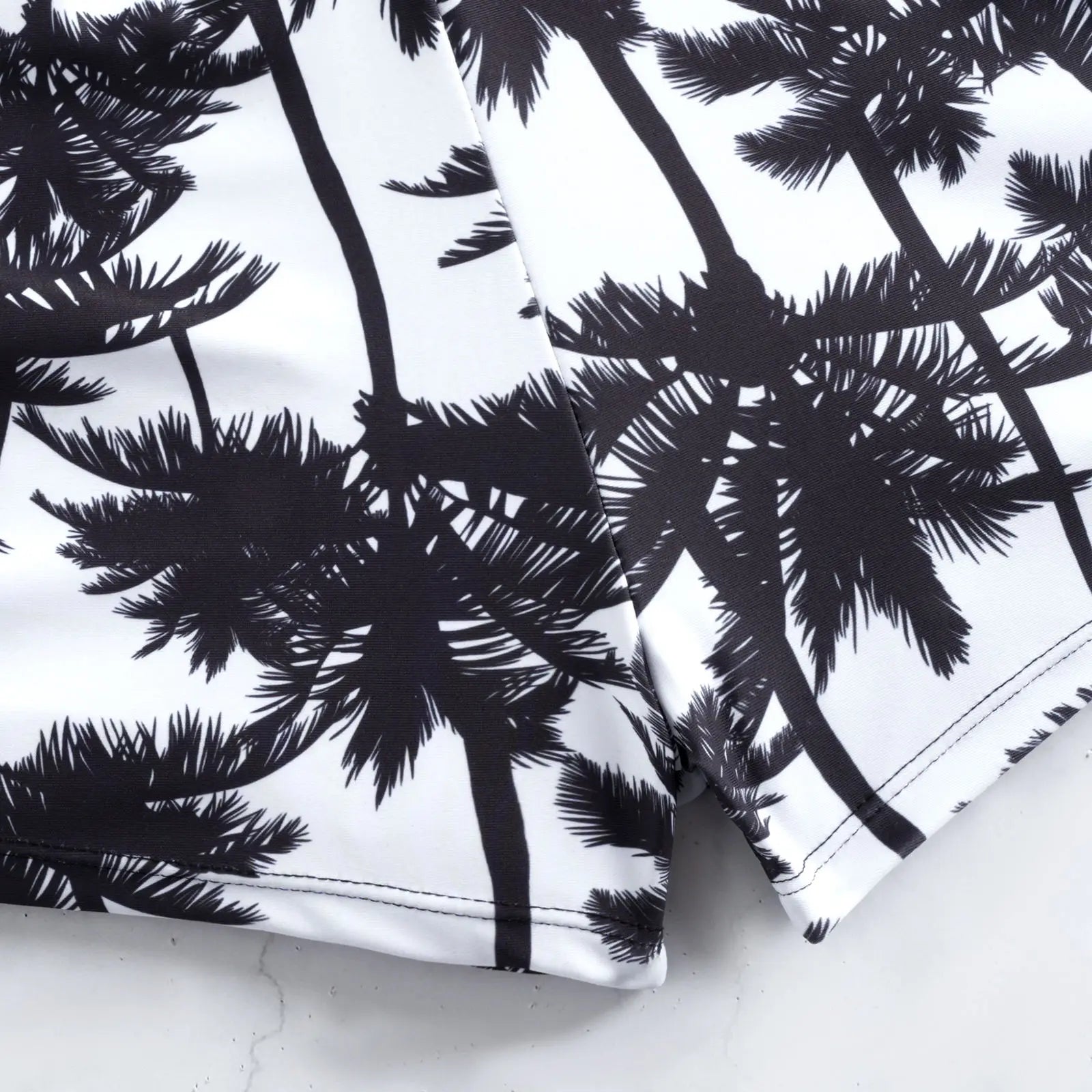 Palm-print swim shorts fabric close-up with drawstring cord and seams.