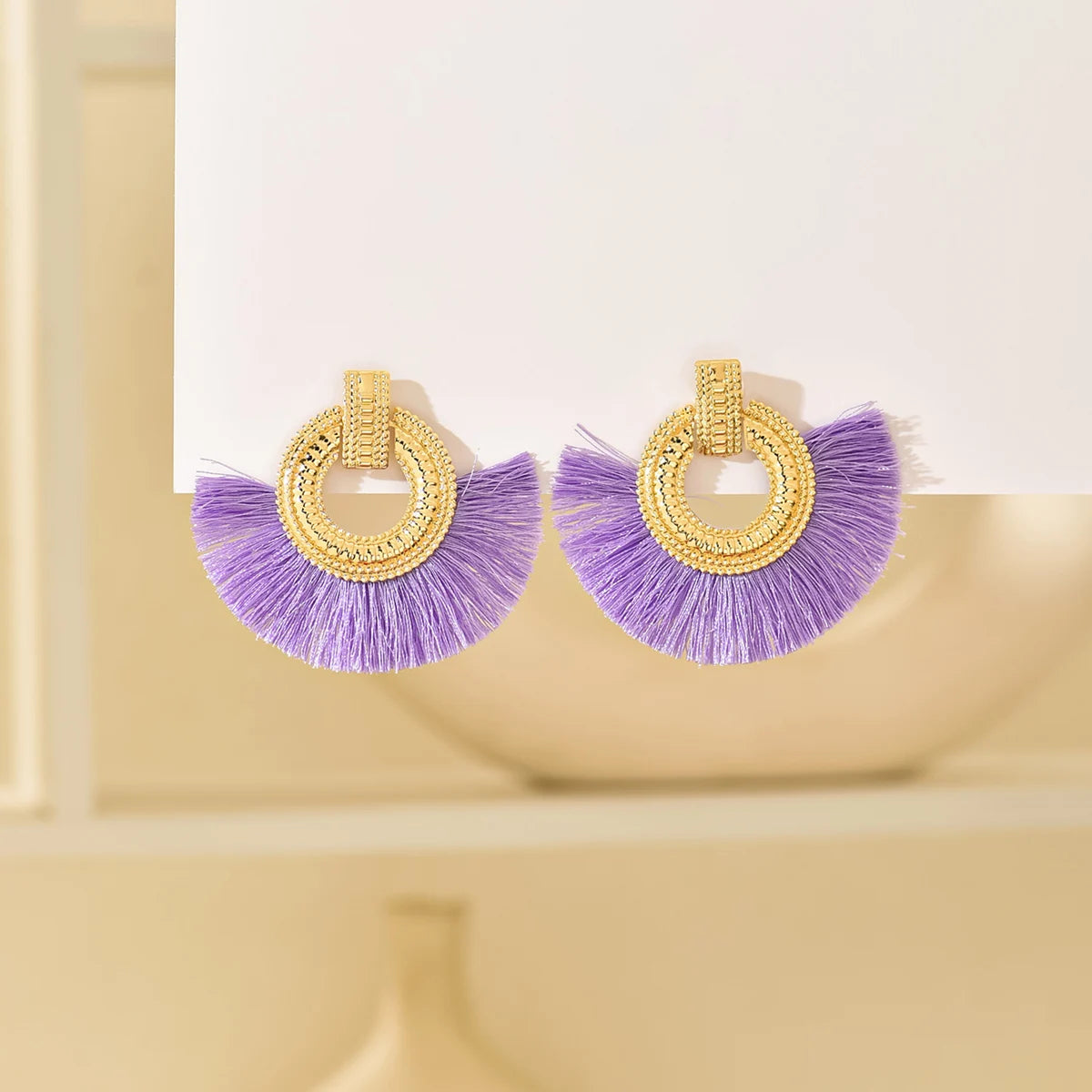 Gold fan stud earrings with purple tassels and circular geometric hoop detail