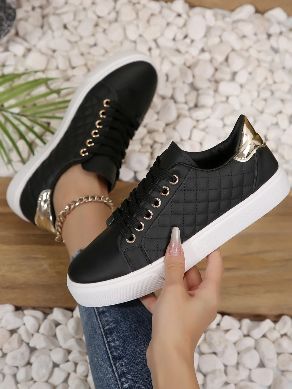 Black quilted lace-up platform sneakers with gold eyelets, side view on feet.