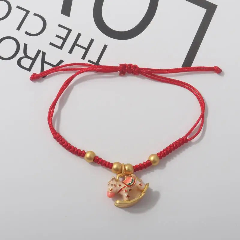 Red rope bracelet with gold beads and a gold horse pendant with colorful details