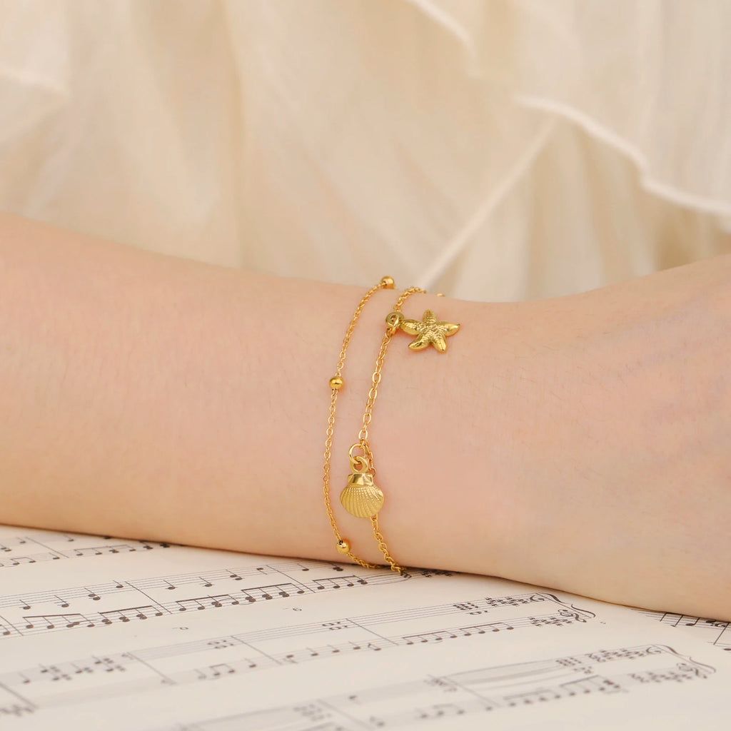 Gold-tone starfish and seashell charm bracelet on wrist with beaded links