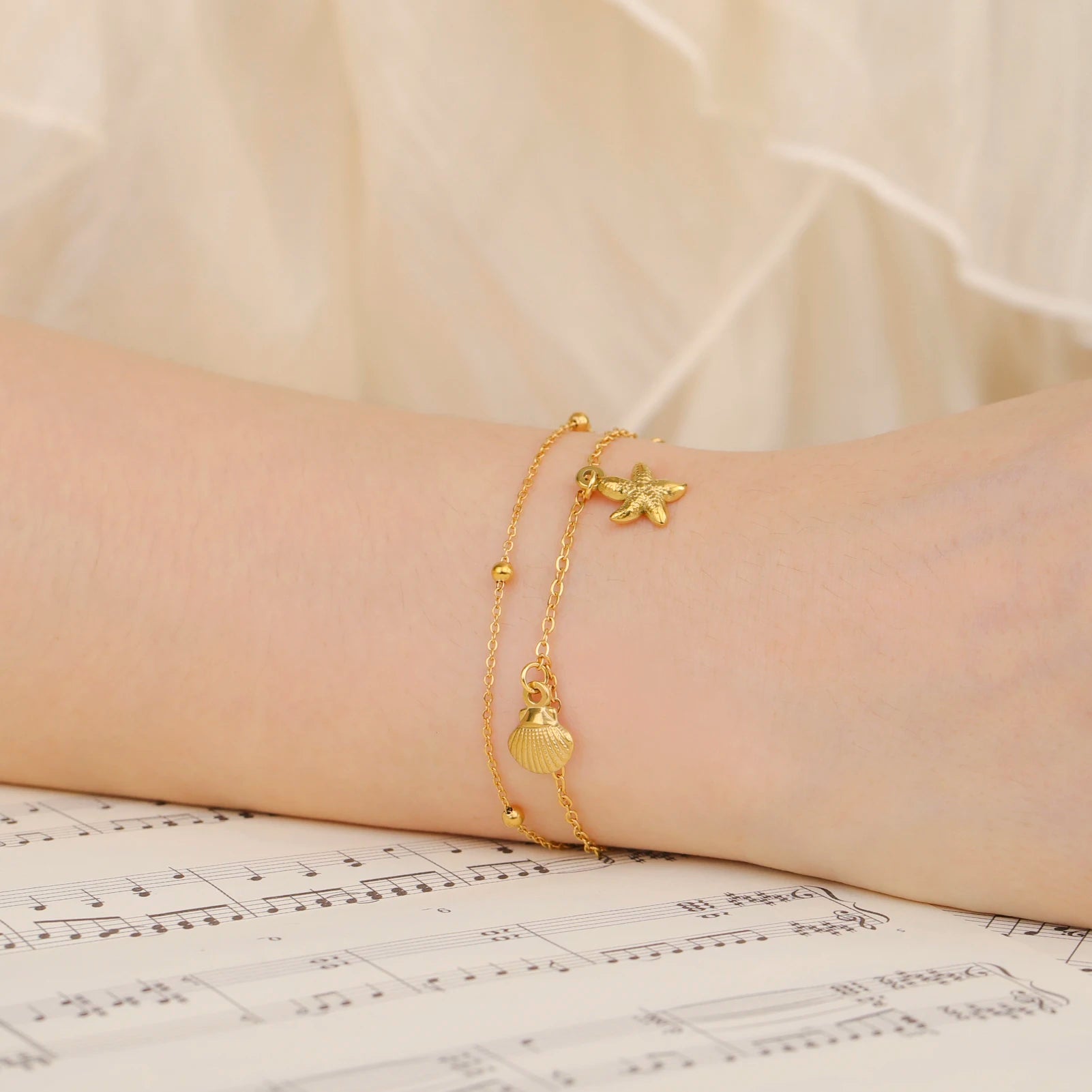 Gold-tone starfish and seashell charm bracelet on wrist with beaded links