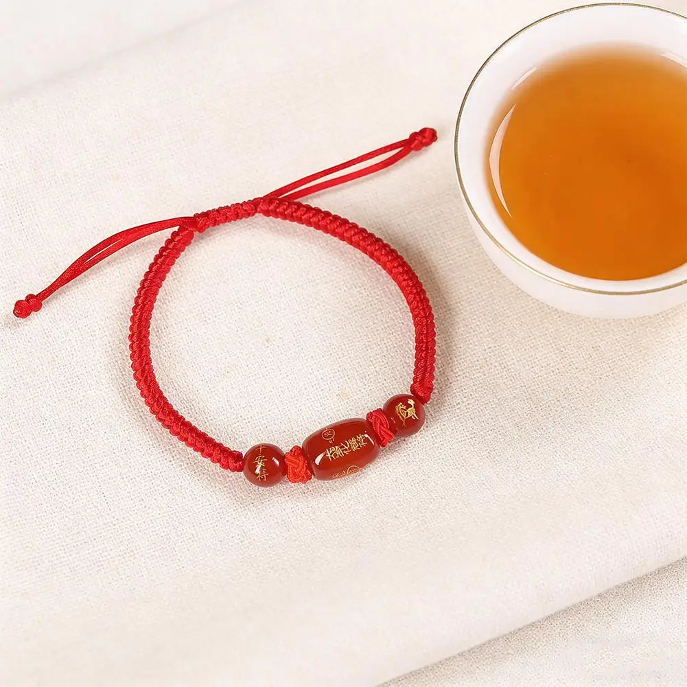 Red braided string bracelet with oval brown bead and small gold-tone symbol charms