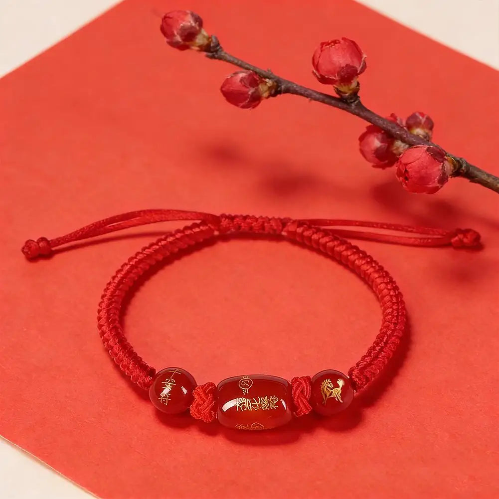 Red braided string bracelet featuring oval brown bead with etched symbols and charms